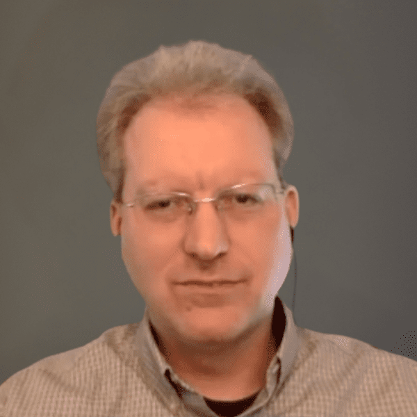 A middle-aged man with glasses and short light hair is wearing a collared shirt and looking at the camera against a plain background.