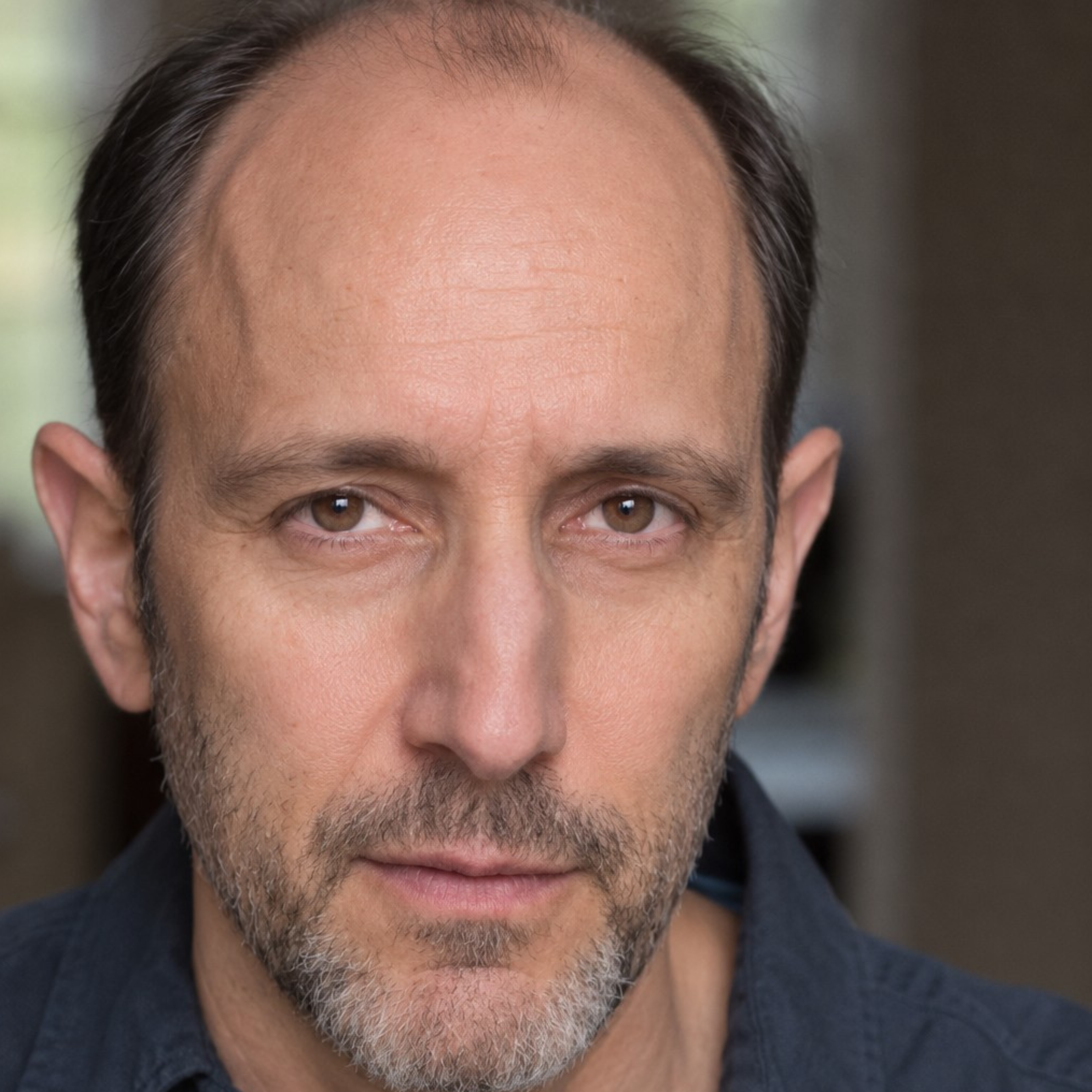 Headshot of a middle-aged man with a receding hairline and salt-and-pepper stubble looking directly at the camera.