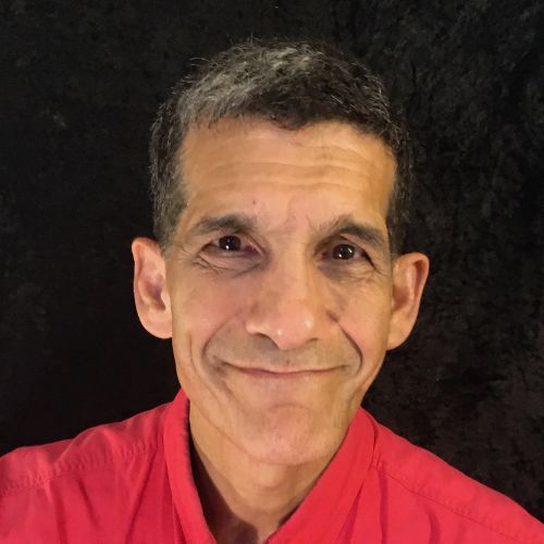 A middle-aged man with short dark hair and a slight smile, wearing a red collared shirt, poses in front of a dark background.