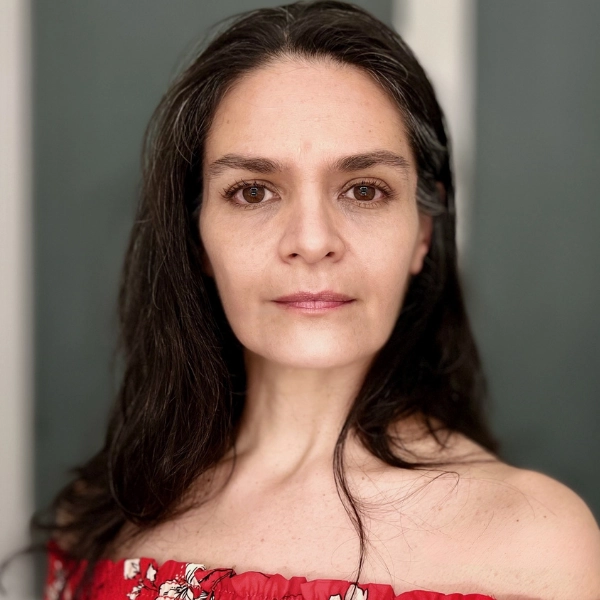 Woman with long dark hair and brown eyes wearing a red off-the-shoulder top, looking directly at the camera with a neutral expression.