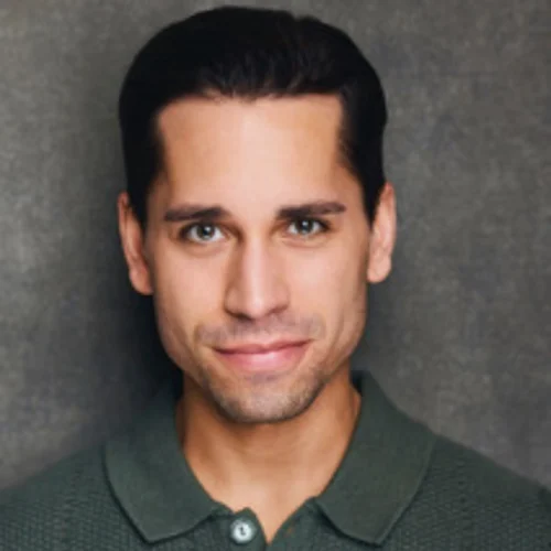 Man with short dark hair wearing a green collared shirt, smiling slightly, in front of a plain gray background.