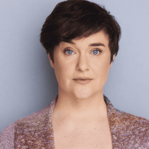 Headshot of a person with short brown hair and blue eyes, wearing a multicolored patterned cardigan.