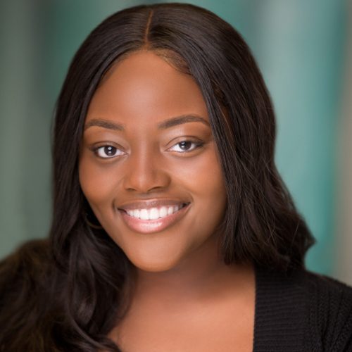 A woman with long dark hair smiles at the camera, wearing a black top with a blurred teal background—perfect for a Deja Holmes bio.
