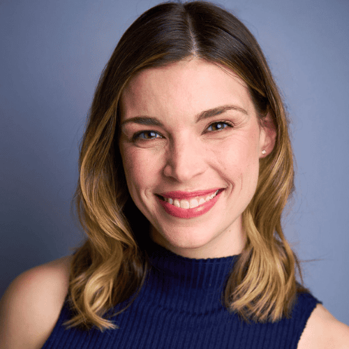 A woman with shoulder-length, light brown hair smiles at the camera against a plain blue background.