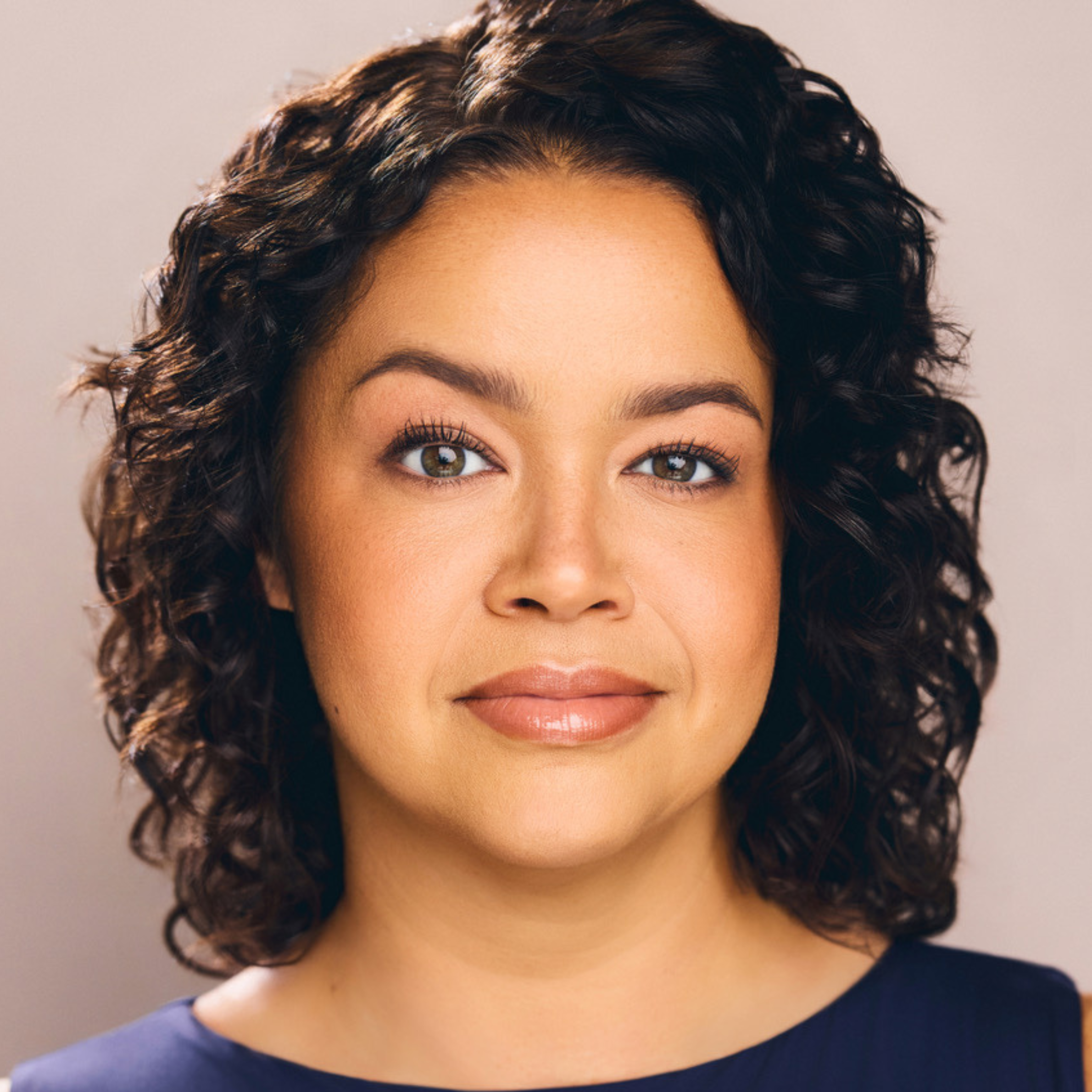 Headshot of a woman with shoulder-length curly dark hair looking directly at the camera.