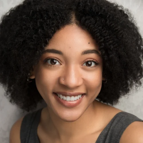 A woman with curly black hair, wearing a sleeveless gray top, smiles at the camera against a light background.