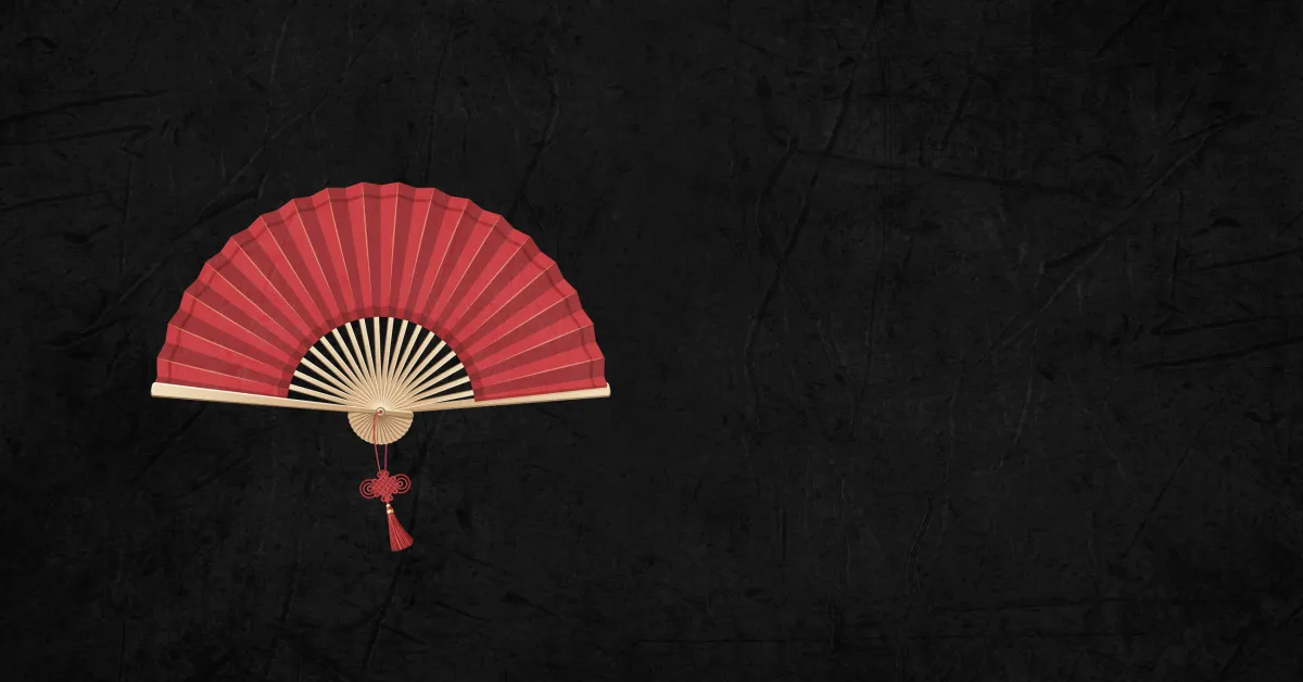 A red folding hand fan with a tassel is open against a plain black textured background, positioned toward the left side of the image.