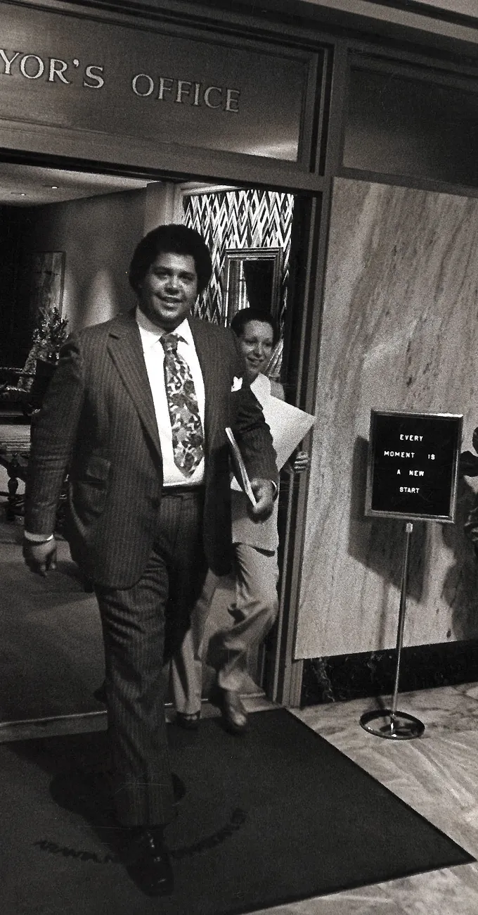 Two people exit an office labeled "MAYOR'S OFFICE." A sign nearby reads, "EVERY MOMENT IS A NEW START." The scene appears to be from a past decade.