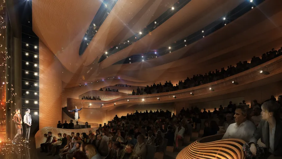 A large audience sits in a modern, architecturally designed theater with layered balconies, watching a performance on stage under dramatic lighting.