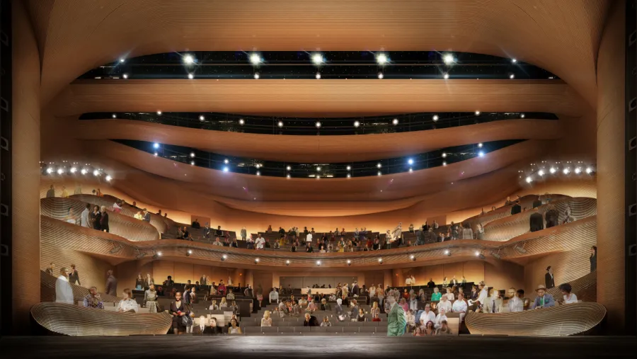 View from a stage looking out at a modern theater auditorium, with multiple tiers of seating and people scattered throughout the audience.