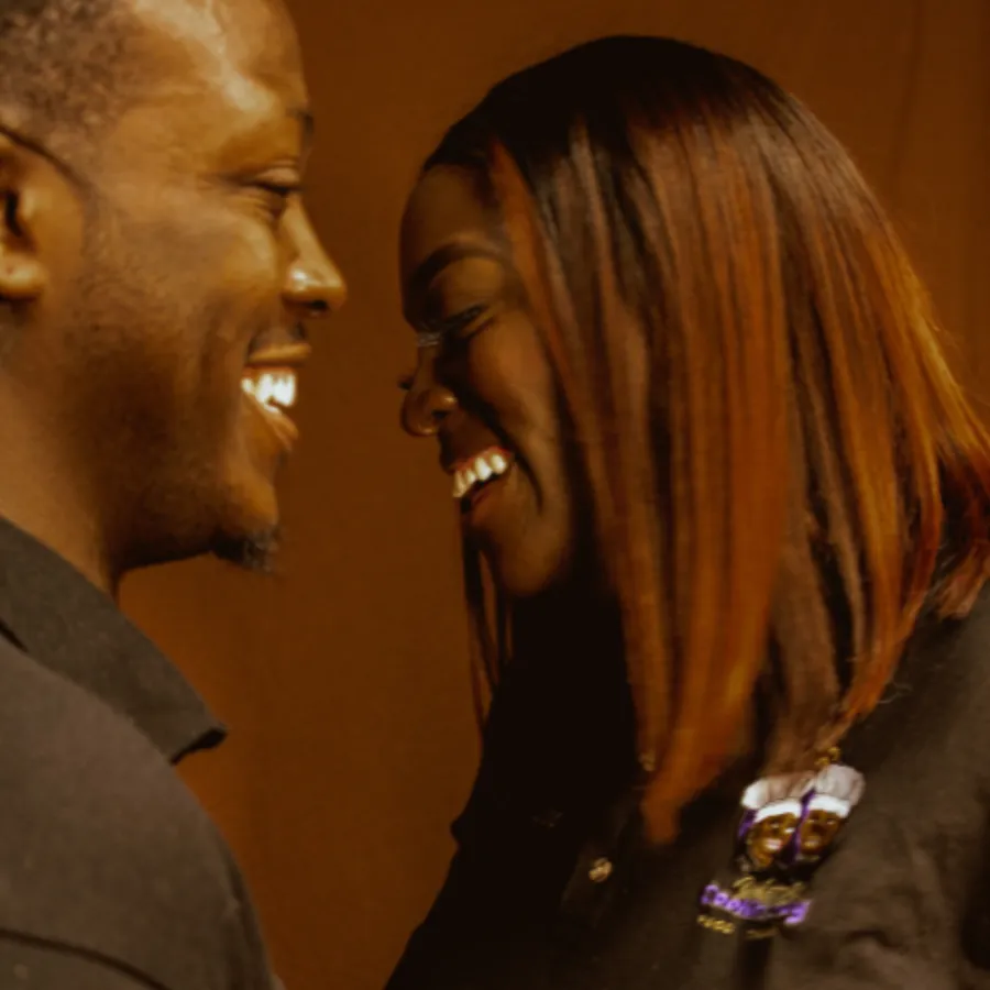 A man and woman stand close together indoors, smiling and laughing while looking at each other.