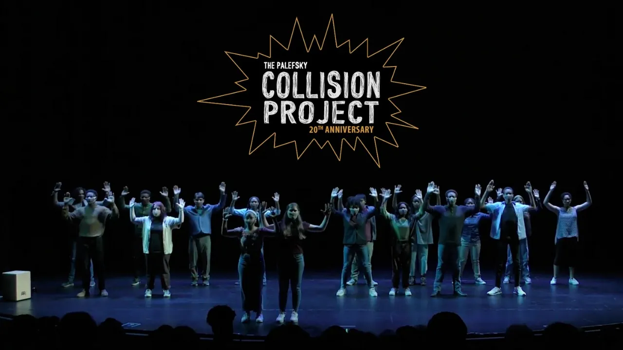 A group of people stand on stage with raised hands beneath a large sign reading "The Alliance's Collision Project 20th Anniversary.