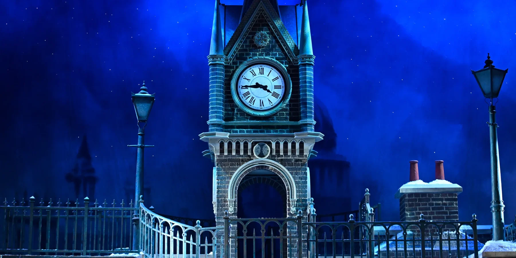 A brick clock tower shows the time as 8:00, surrounded by iron railings and lampposts, with a snowy rooftop and night sky in the background.