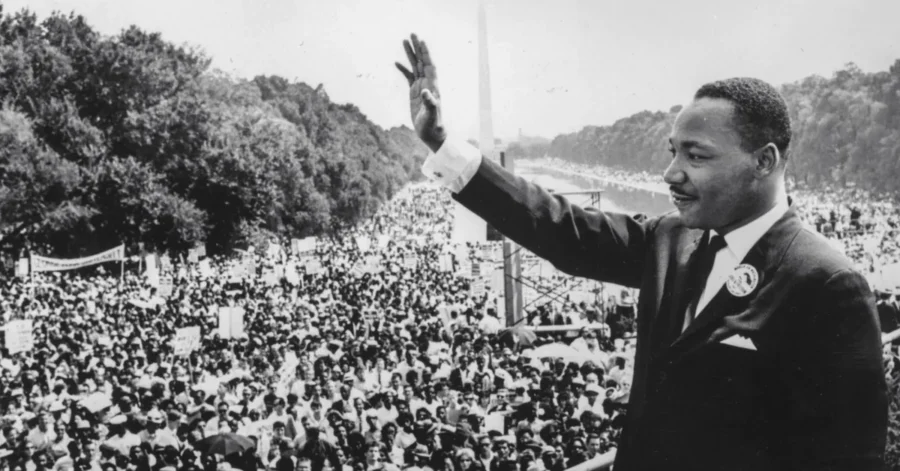 A man in a suit waves to a large crowd gathered outdoors near the Washington Monument in Washington, D.C.