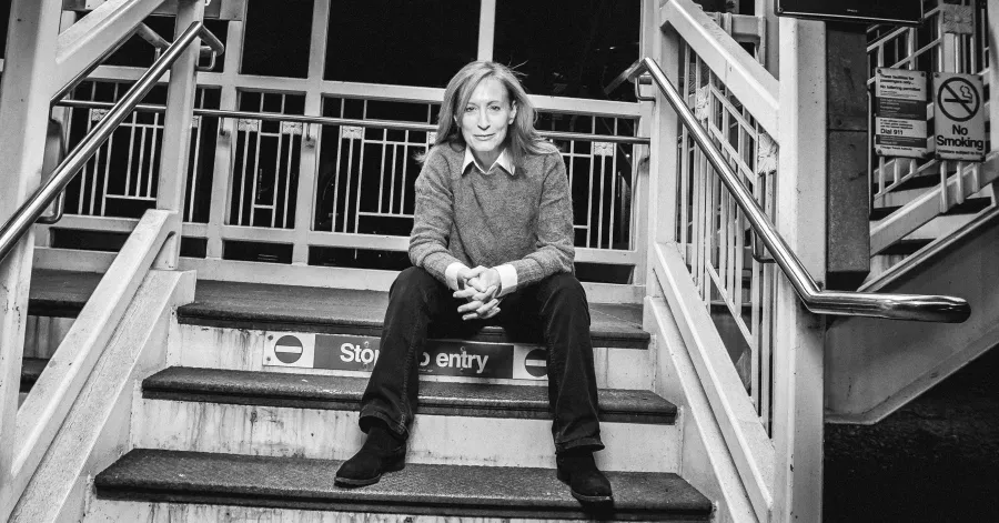 A person sits on stairs marked “Stop, no entry” at a transit station, with railings and “No Smoking” signs visible in the background.