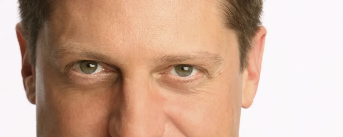 A close-up of a man's face, focusing on his green eyes and upper cheeks, with short brown hair and a neutral expression.
