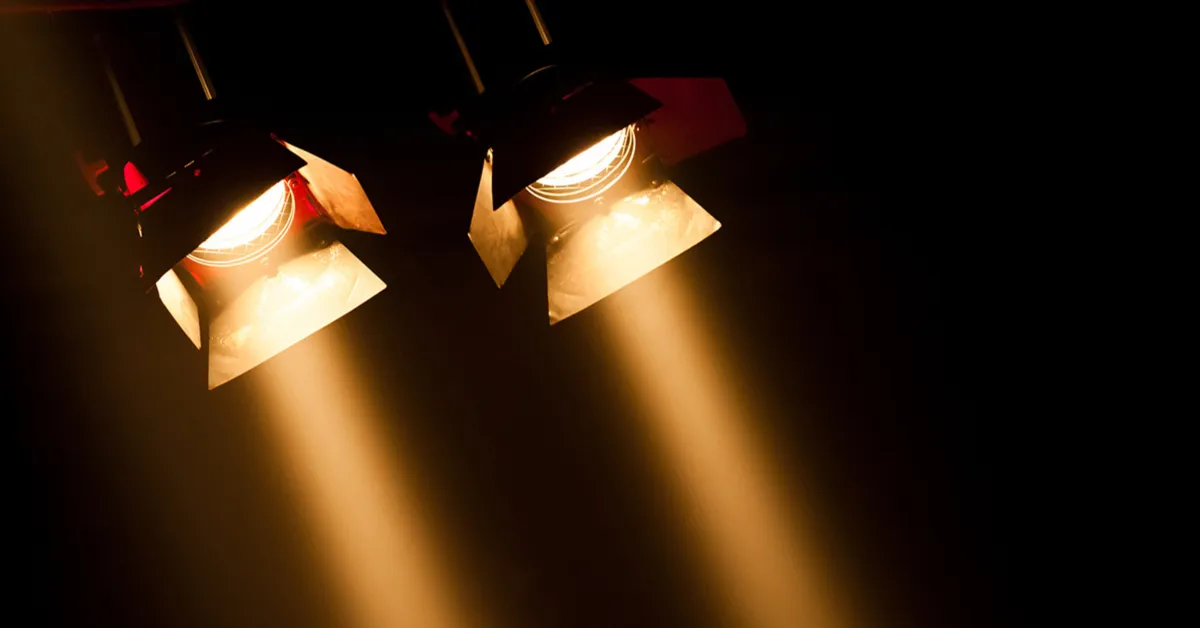 Two stage spotlights shining bright beams of light downward in a dark setting.