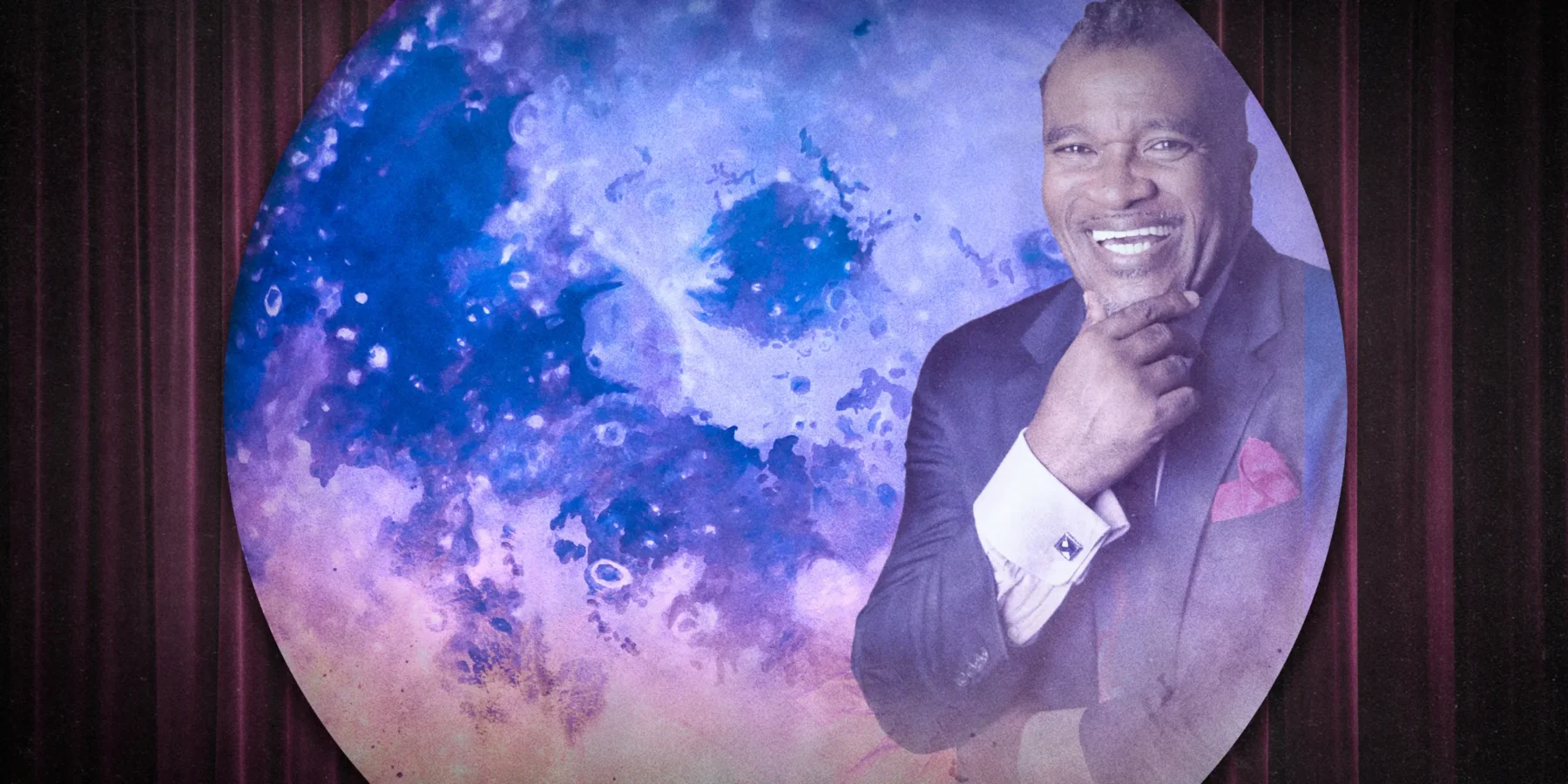 A man in a suit smiles and poses with his hand on his chin in front of a large circular blue and purple abstract background.