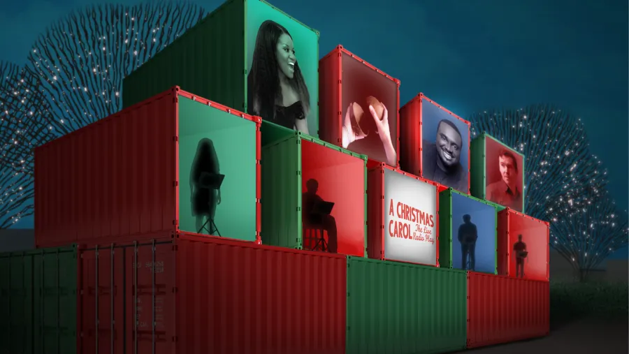 A stack of red and green shipping containers displays projected images of people and the text "A Christmas Carol" against a night sky with illuminated trees.