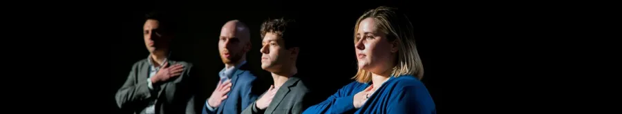 Three people stand in a row, each with their right hand over their heart, facing forward with serious expressions against a dark background.