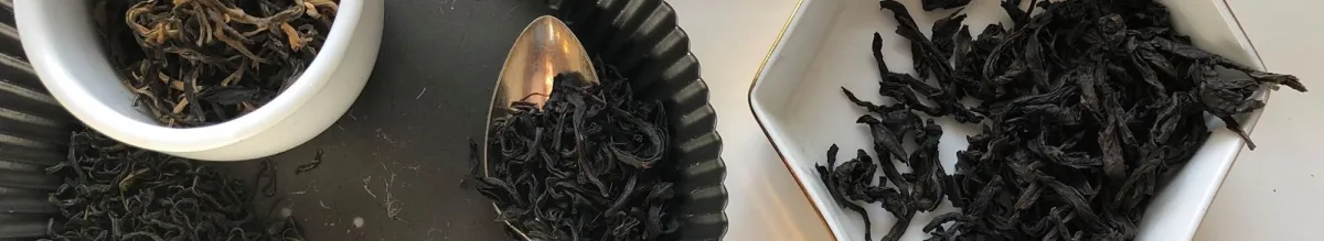 Loose leaf black tea displayed in a white bowl, a silver spoon, and a white dish on a dark surface.