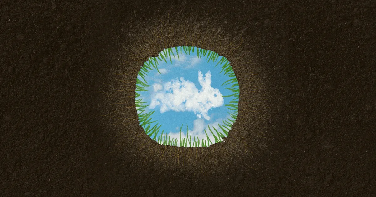 A hole in the ground with grass around the edge reveals a view of blue sky and clouds above.