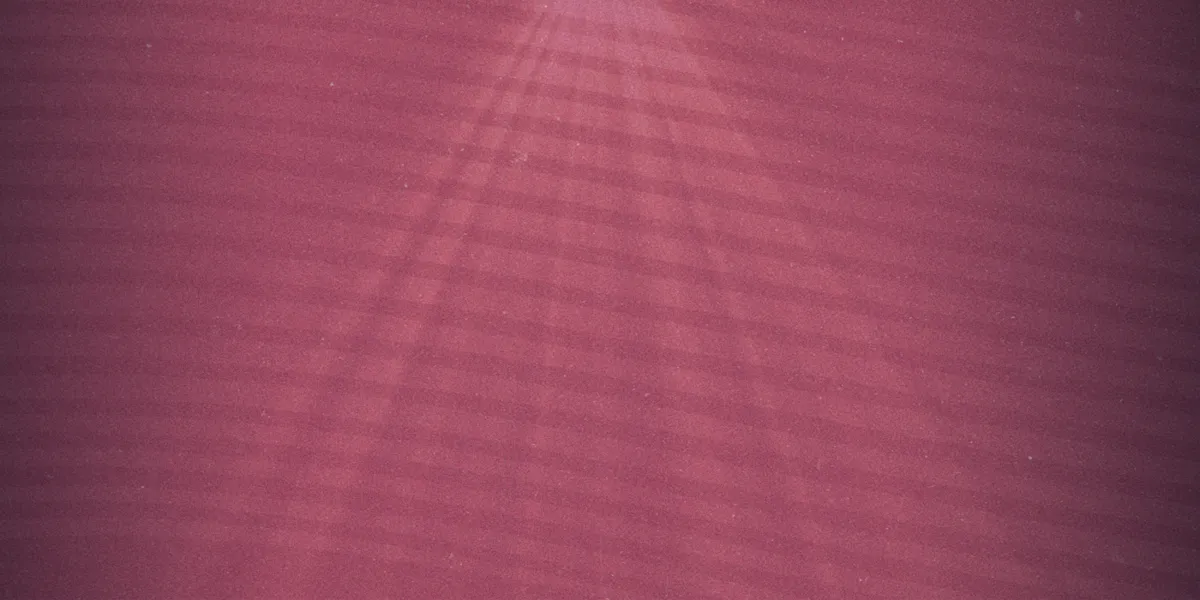 Pink textured surface with diagonal light and shadow lines radiating from a bright spot near the top of the image.