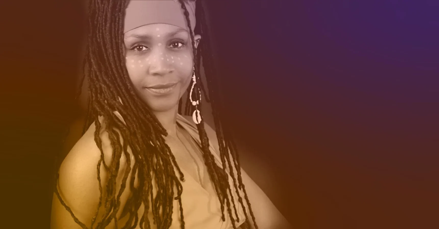 A woman with long, styled dreadlocks, wearing a headband and beaded earrings, faces the camera with a faint smile. Her face is adorned with white dotted markings.