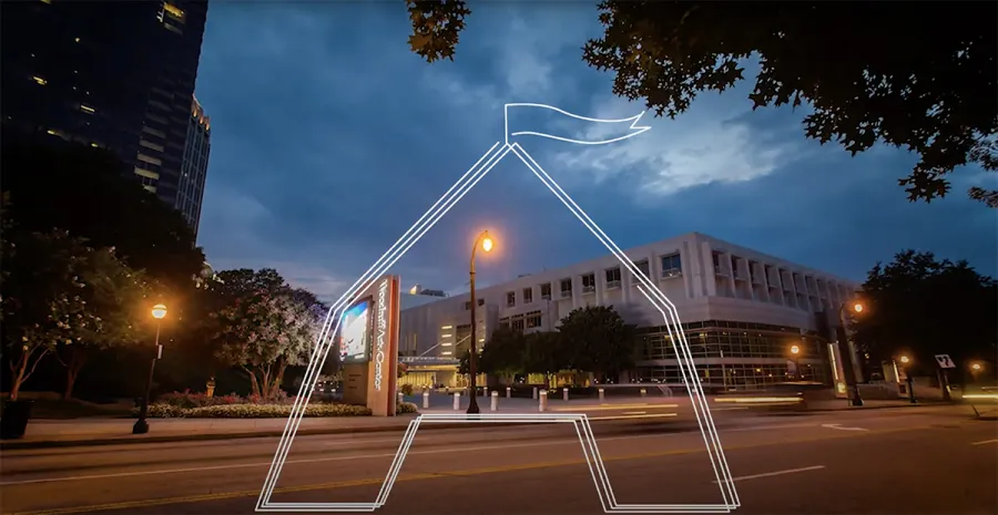 A city street at dusk with a modern building in the background and a white outlined graphic of a house with a flag overlayed on the image.