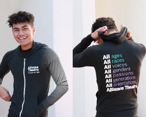 A person wears a black hoodie with "Alliance Theatre" on the front. The back lists “All ages, All races, All voices, All genders, All passions, All generations, All orientations.”.