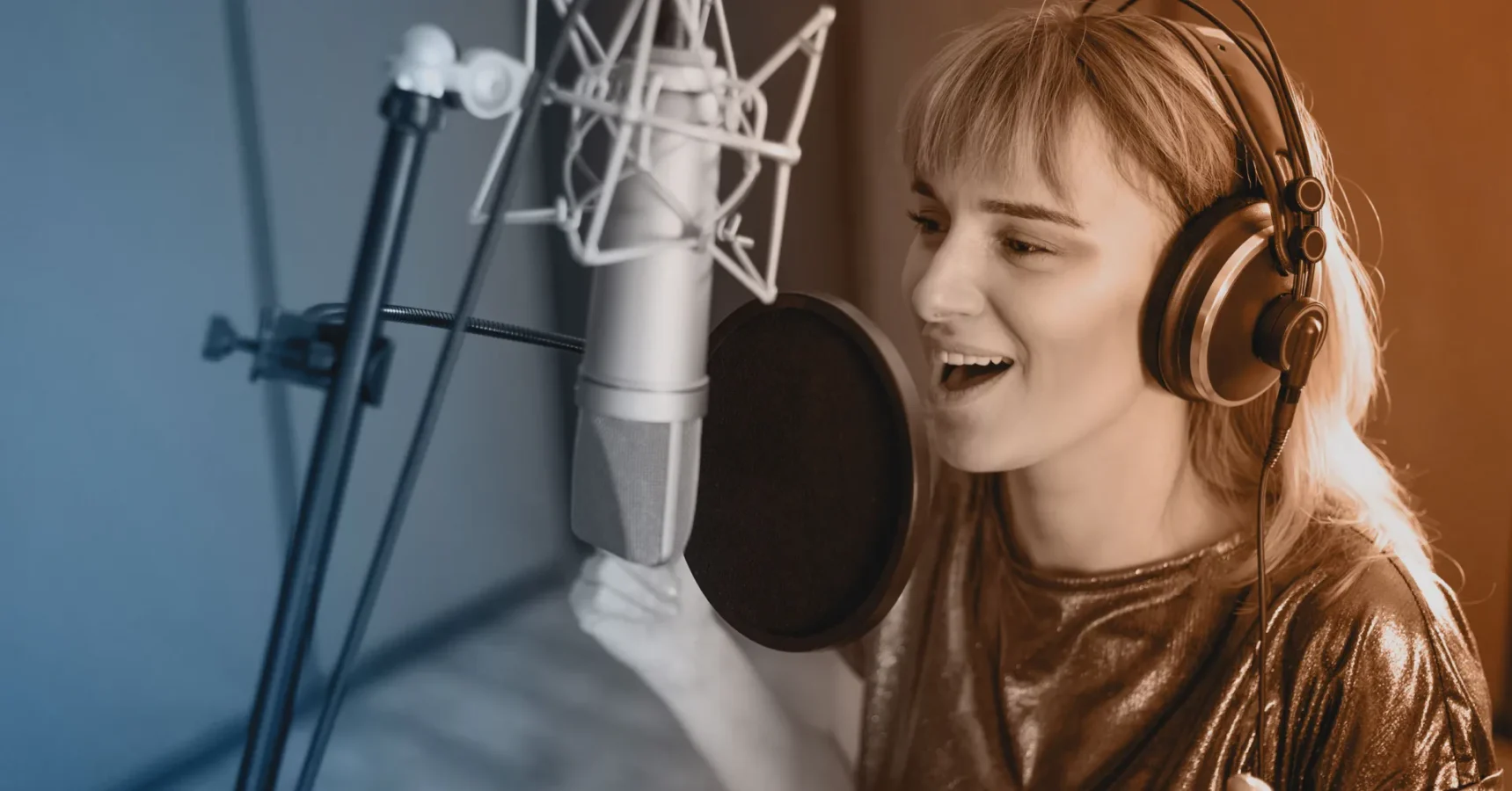 A person wearing headphones sings into a microphone in a recording studio.