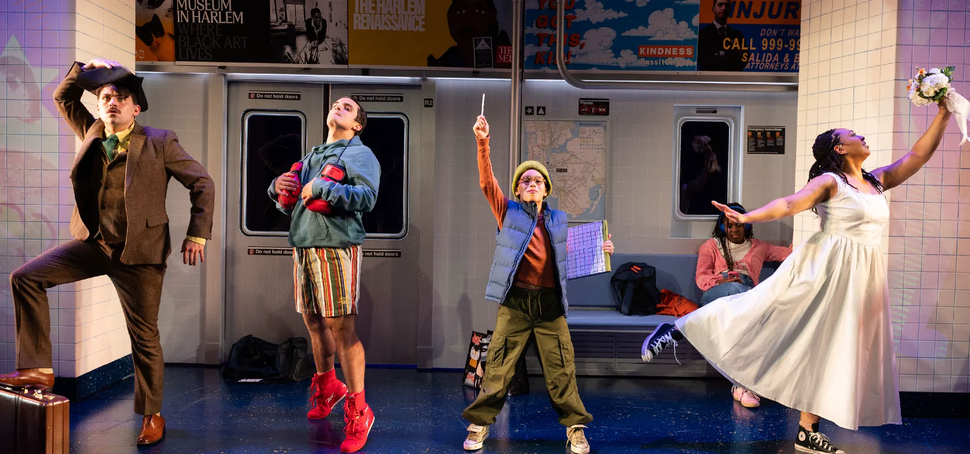 Four actors in colorful costumes pose dramatically on a stage set designed to look like a subway train, with city-themed advertisements on the walls.