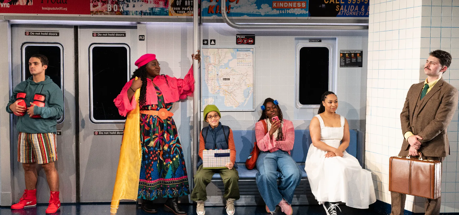 Six people in varied colorful outfits sit and stand inside a subway car, each engaged in different activities, with a subway map and posters visible behind them.