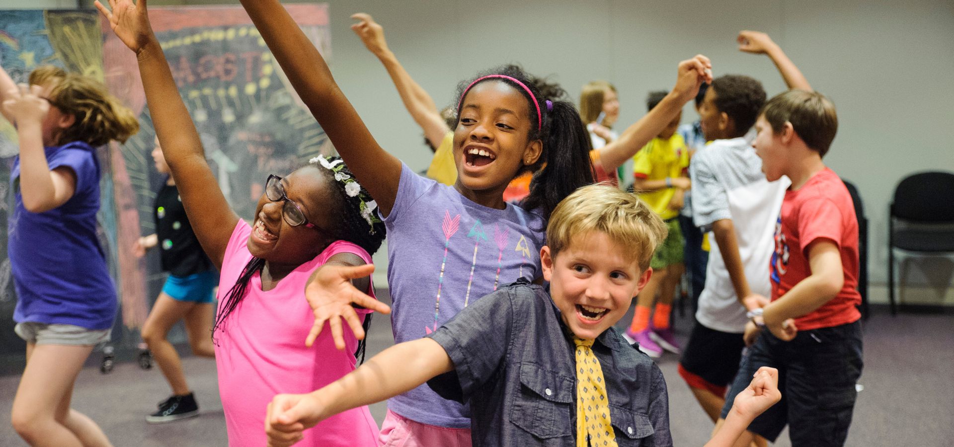 A group of children, smiling and posing with energetic gestures, participate in an indoor group activity.