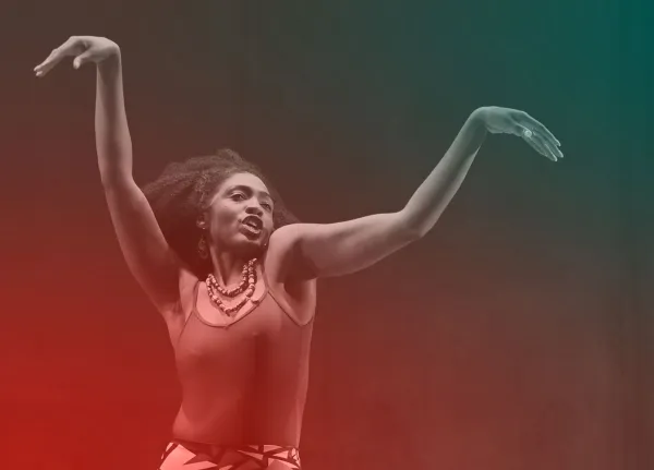 A woman with raised arms poses expressively against a dark background with red and green gradient lighting. She wears a sleeveless top, beaded necklace, and patterned skirt.