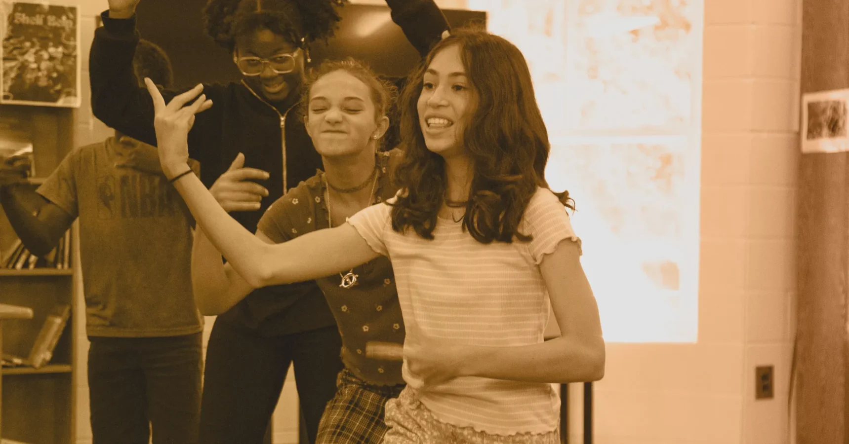 Three teens stand together indoors, smiling and dancing with their arms raised in expressive gestures.