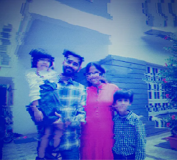 A family of four poses outside a house; the image appears distorted with digital glitches.