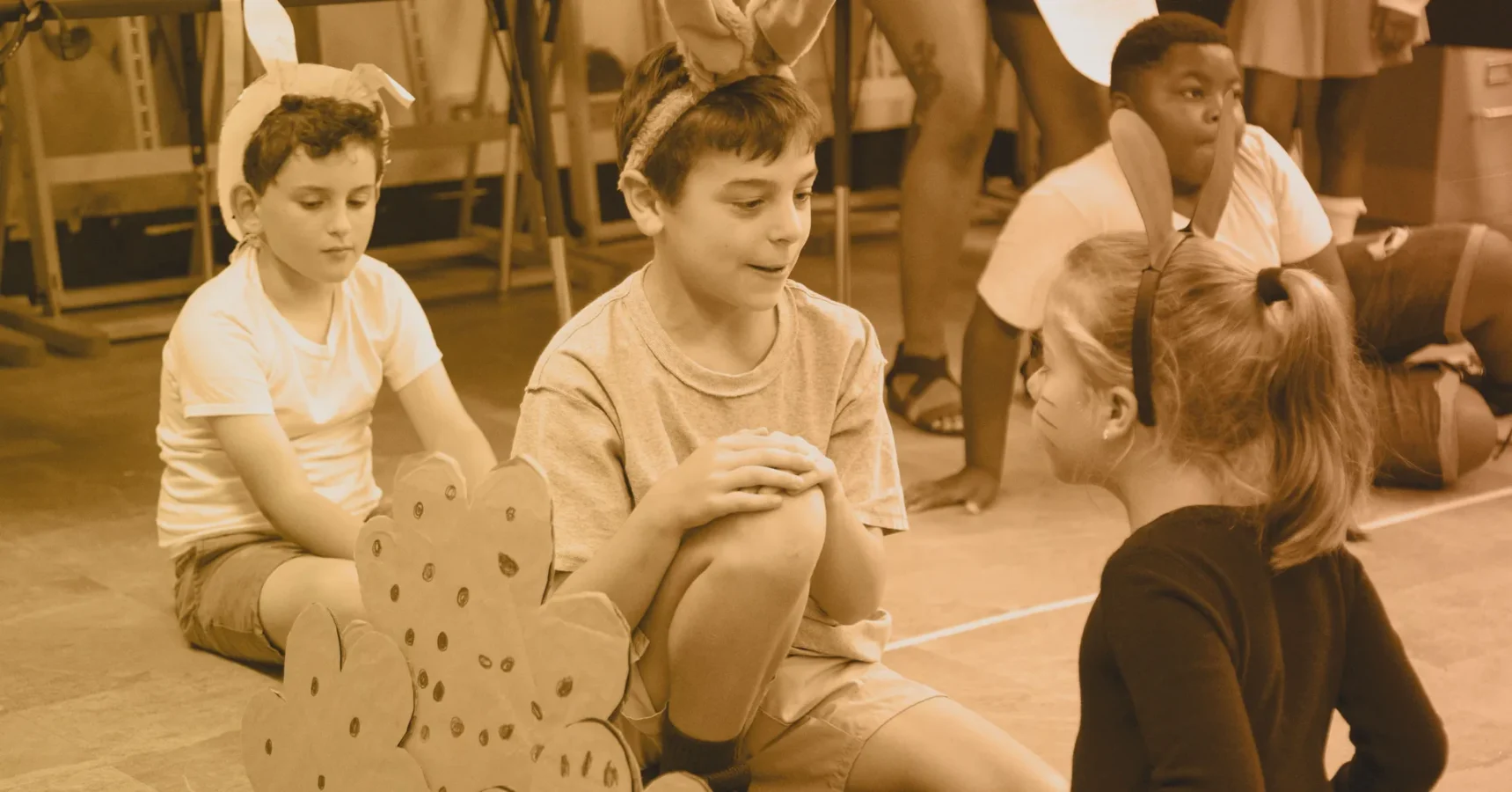 Children wearing bunny ear headbands sit and interact with each other on the floor during what appears to be a play or group activity.