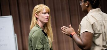 Two people are having a serious conversation indoors; one is speaking with hand gestures while the other listens attentively.