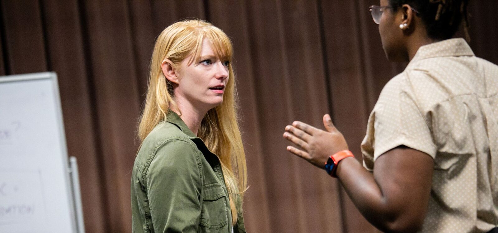 Two people are having a serious conversation indoors; one is speaking with hand gestures while the other listens attentively.