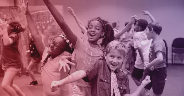 A group of children enthusiastically dance and pose together in a classroom or activity room.