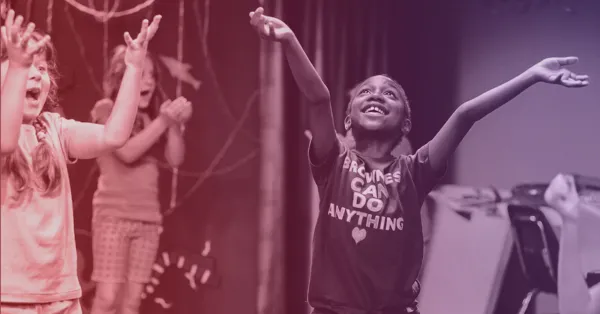 Three children stand with arms raised and smiling; the child in front wears a shirt that says "Girls can do anything.