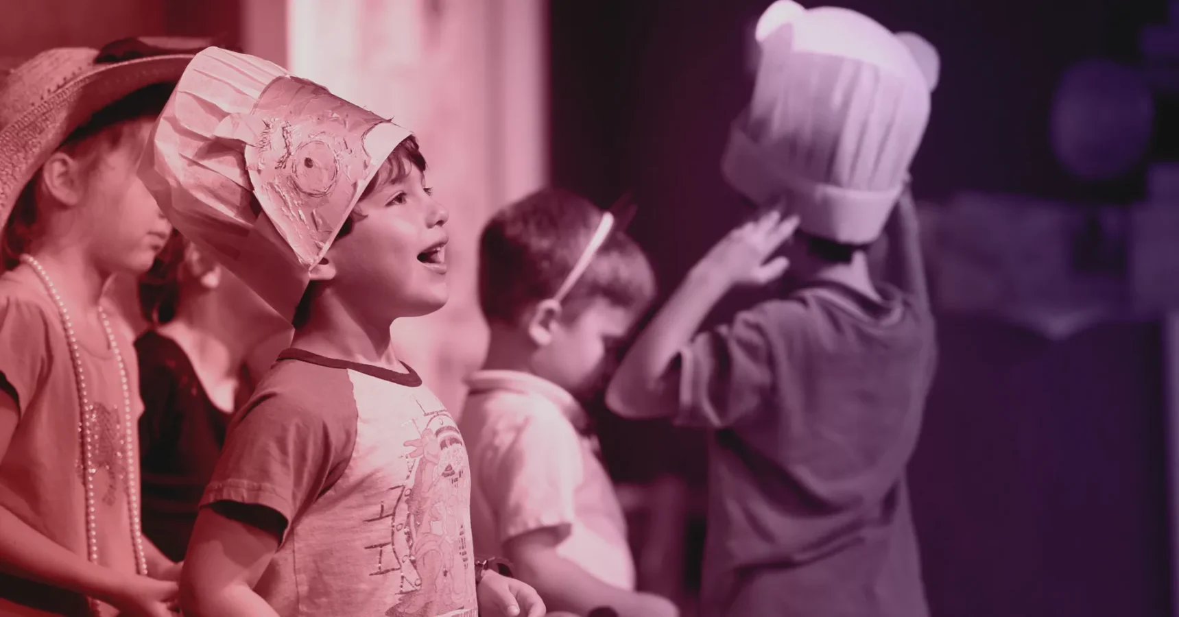 Children wearing costumes participate in an indoor activity; one child in front sings while others are focused on their own tasks.