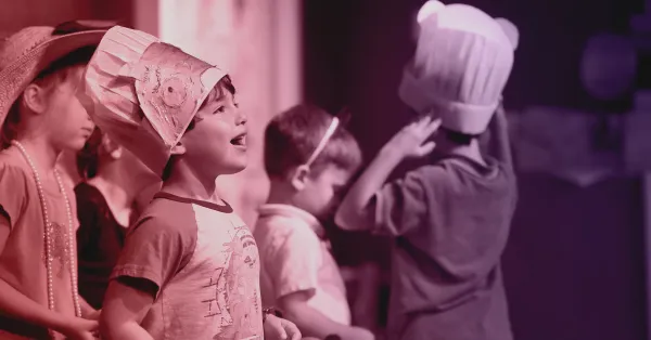 Four children wearing costumes and hats stand in a row, participating in what appears to be a play or performance.