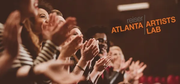 A diverse group of people sit in an audience, clapping. The text "Reiser Atlanta Artists Lab" is displayed on the wall in the background.