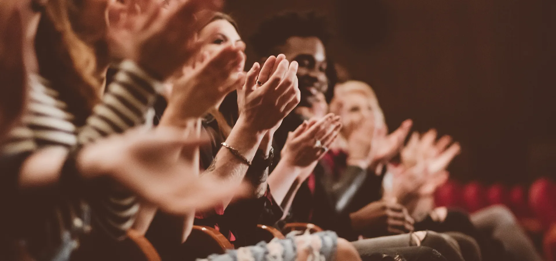 A group of people sitting in an audience clapping, with hands in focus and faces blurred in the background.