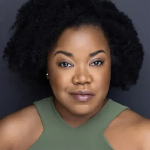 A woman with natural curly hair and medium-dark skin wears a sleeveless olive green top, looking directly at the camera against a plain dark background.