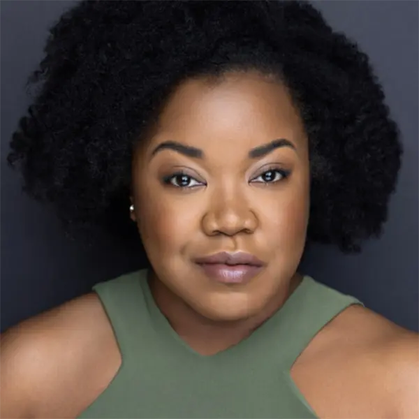 A woman with natural curly hair and medium-dark skin wears a sleeveless olive green top, looking directly at the camera against a plain dark background.