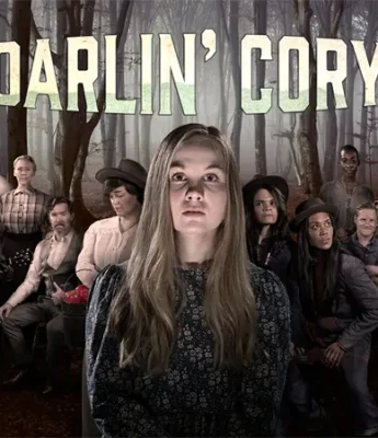 A young woman stands in front of a group of people in old-fashioned clothing in a foggy forest, with the title "Darlin' Cory" displayed above them.