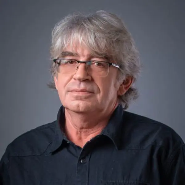 A middle-aged man with gray hair and glasses wearing a black button-up shirt poses against a plain gray background.